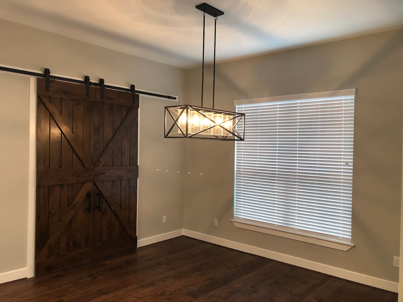 Black linear cage chandelier installed over a dining space beside a wood barn door